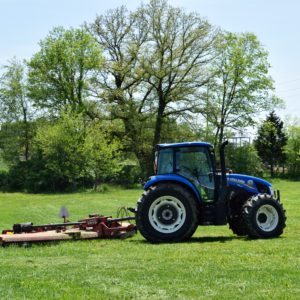 A tractor is parked in the grass near trees.